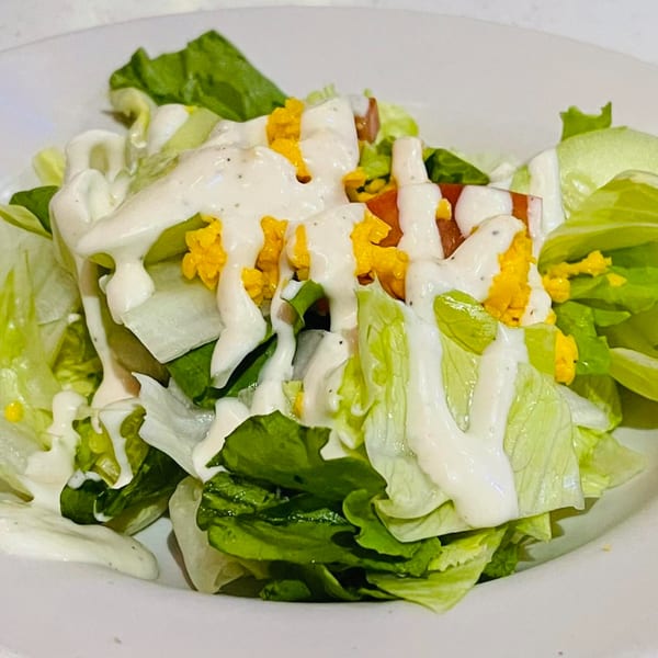 A fresh side salad with crisp lettuce, diced tomatoes, shredded cheese, and creamy ranch dressing.