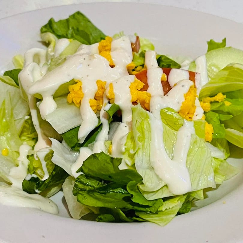 A fresh side salad with crisp lettuce, diced tomatoes, shredded cheese, and creamy ranch dressing.