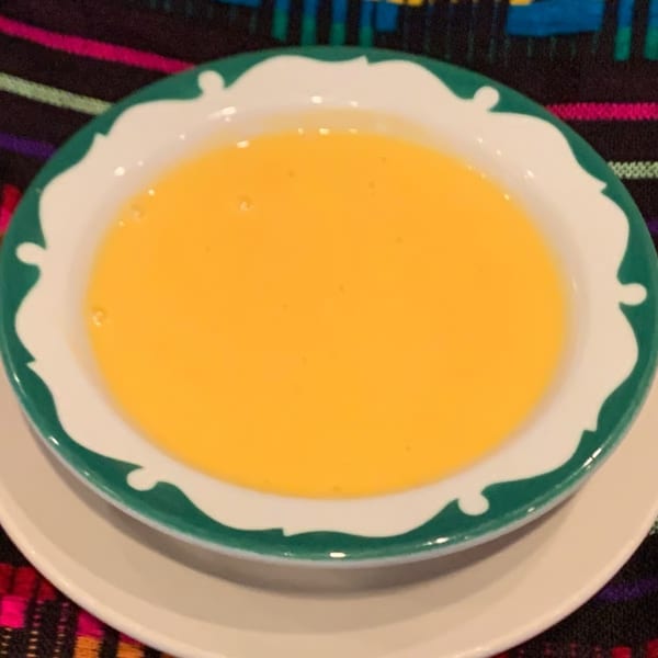 A bowl of bright yellow queso dip with a green and white rim, on a colorful patterned tablecloth.