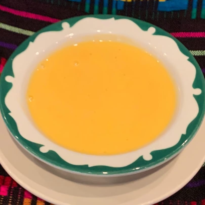 A bowl of bright yellow queso dip with a green and white rim, on a colorful patterned tablecloth.