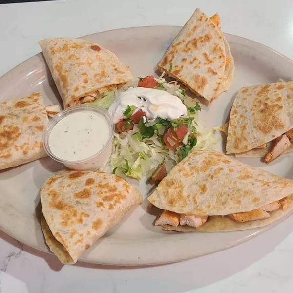 Chicken quesadillas with sour cream, salsa, and shredded lettuce on a white plate.