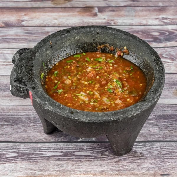 Freshly made salsa in a traditional molcajete, garnished with cilantro, on a wooden table.